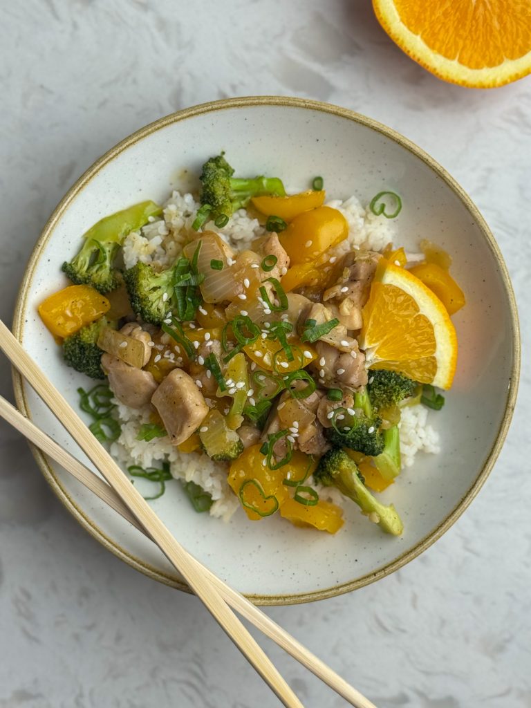 Orange chicken stir fry and white rice in a bowl with chopsticks.